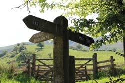 Wooden gates, a signpost, and countryside on the Mam Tor Circular Walking route.