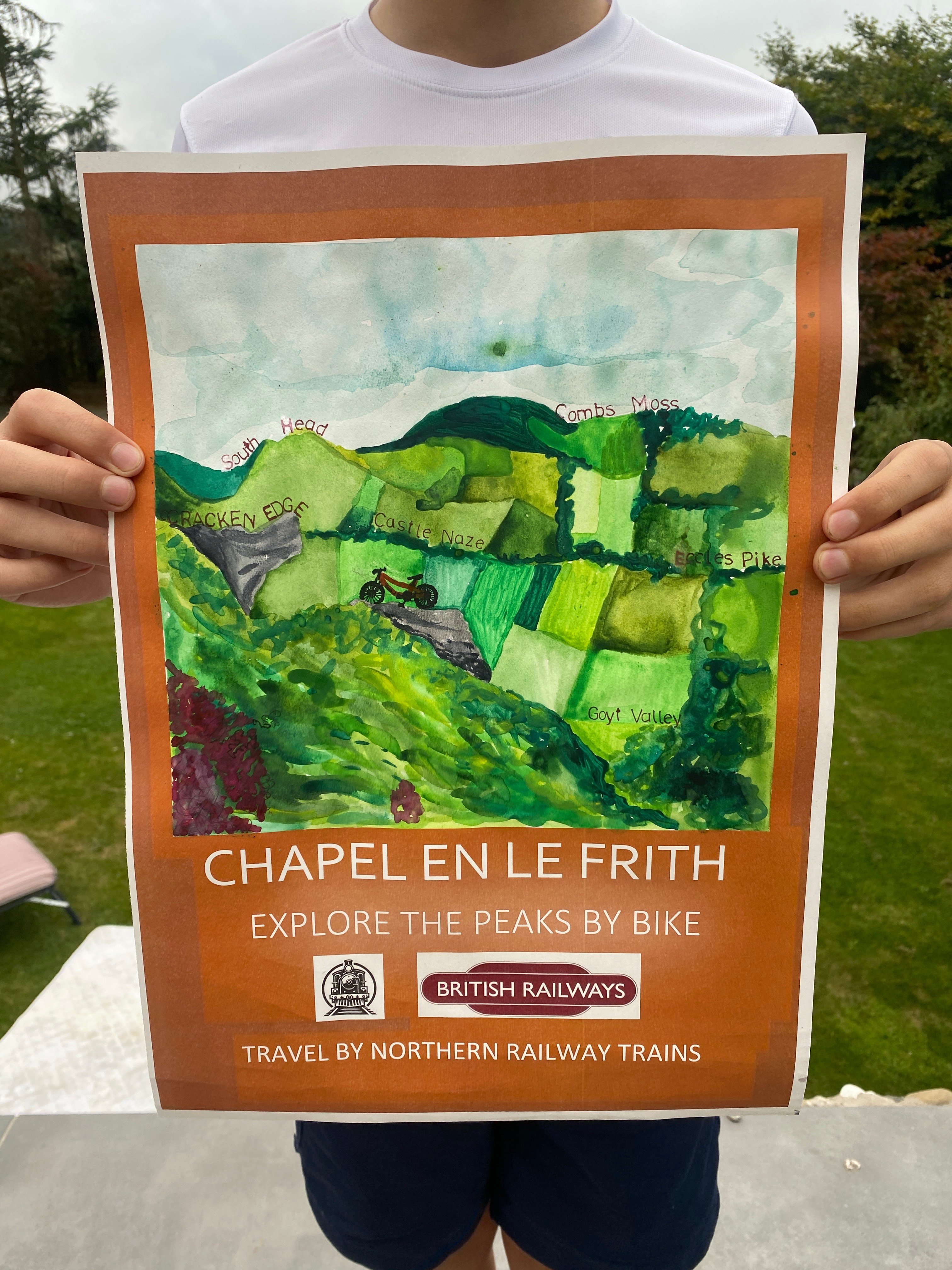 A boy holding up winning artwork. Artwork shows a scenic view of the peaks with green hills and fields.