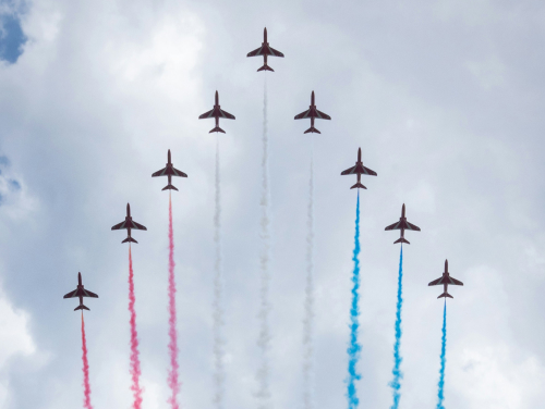 Nine jets flying in formation across a cloudy sky, trailing red, white and blue smoke.