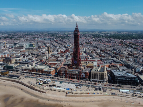 Aerial view of Blackpool’s seafront, featuring Blackpool Tower, surrounding buildings and the sandy beach.