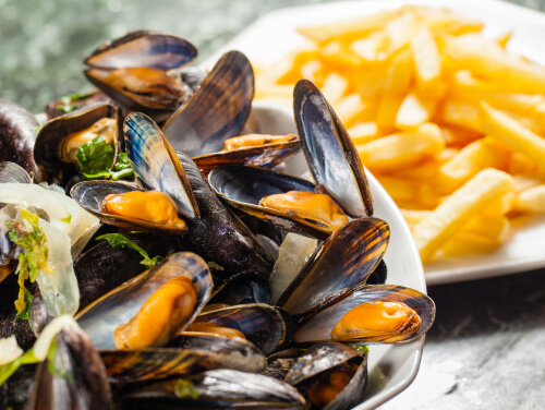 A bowl of mussels with a plater of chips next to it.