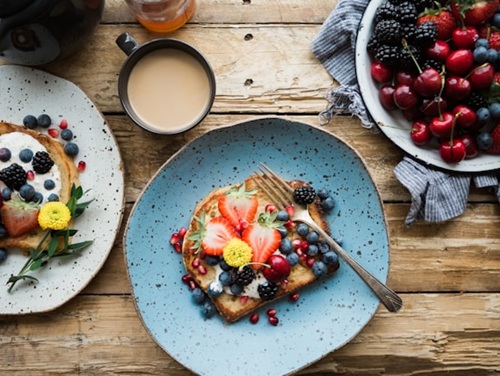 Toast topped with strawberries, blueberries, and blackberries on a plate, with a cup of coffee on a wooden table.