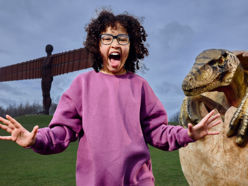 A girl playfully pretending to scream in front of a statue of a dinosaur hatching from an egg.