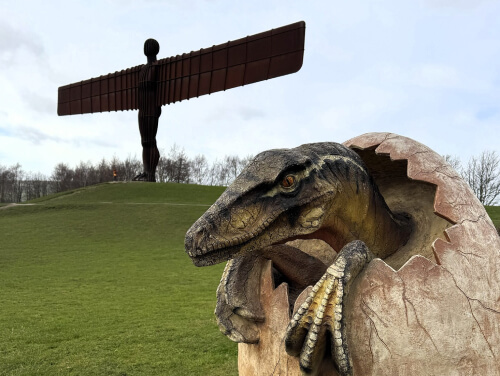 A dinosaur hatching from an egg in front of the Angel of The North