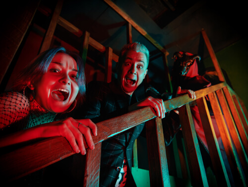Frightened visitors lean over a wooden railing at a Halloween attraction.