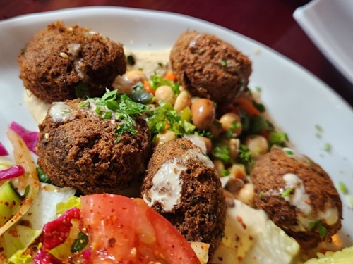 Falafel balls served with chickpeas, salad, and sauce on a plate.