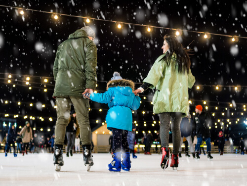A mum and dad hold their daughter's hands while ice skating.