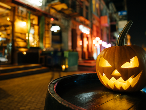 Pumpkin lantern sitting on a barrel on a street at night