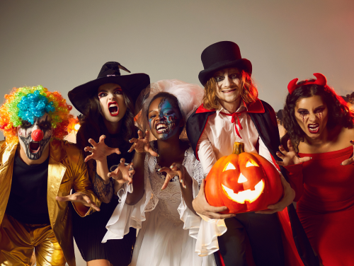 Five people dressed up in Halloween costumes with one holding a pumpkin lantern