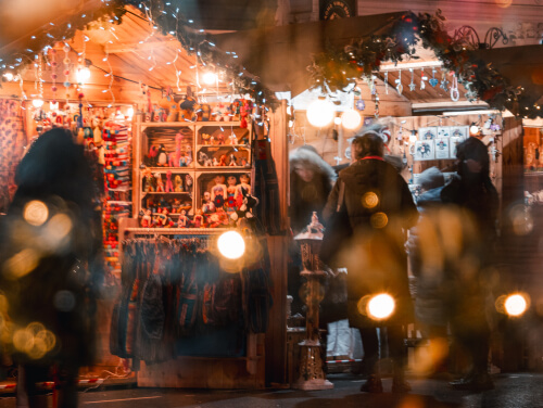 A series of lit up Christmas Market lodges featuring gifts and trinkets.
