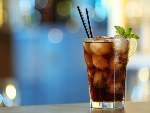 Vodka mixed with coke and garnished with a slice of lime and mint atop a bar table.