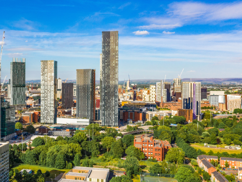 Manchester skyline with modern high-rise buildings and green spaces in the foreground.