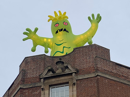 A green, illuminated, inflatable monster with flailing arms on top of a building as part of the Lincoln Monster Invasion event.