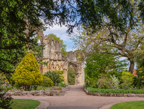 A scenic view of a historic stone archway surrounded by lush greenery and a well-maintained garden path.