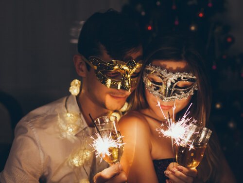 Couple with white wine and sparklers wearing masquerade masks.