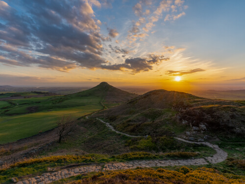 The image shows a scenic view of the North York Moors at sunset, with rolling hills, a winding path, and a glowing sky.
