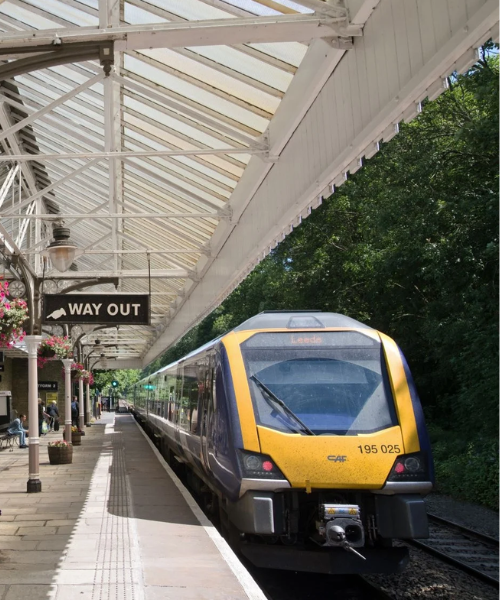 Train stopped at a station platform beneath a white canopy, with a “Way Out” sign overhead.