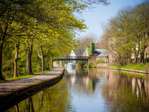 Tree-lined canal with a boat and bridge on a sunny day.