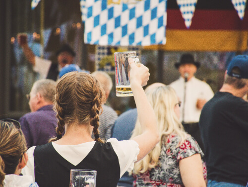 A girl wearing a drundl dress with her hair in plaits, toasting a beer at Oktoberfest.