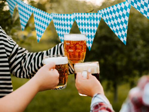 Friends cheering with three beers in front of festival flags.