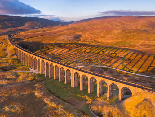 Ribblehead Viaduct stretching across the Yorkshire Dales, surrounded by sweeping moorland in rich orange and golden autumn colours under an October sky.