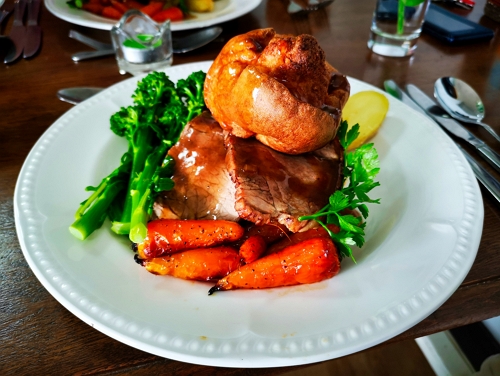 Roast beef dinner with Yorkshire pudding, carrots, broccoli and gravy on a white plate.