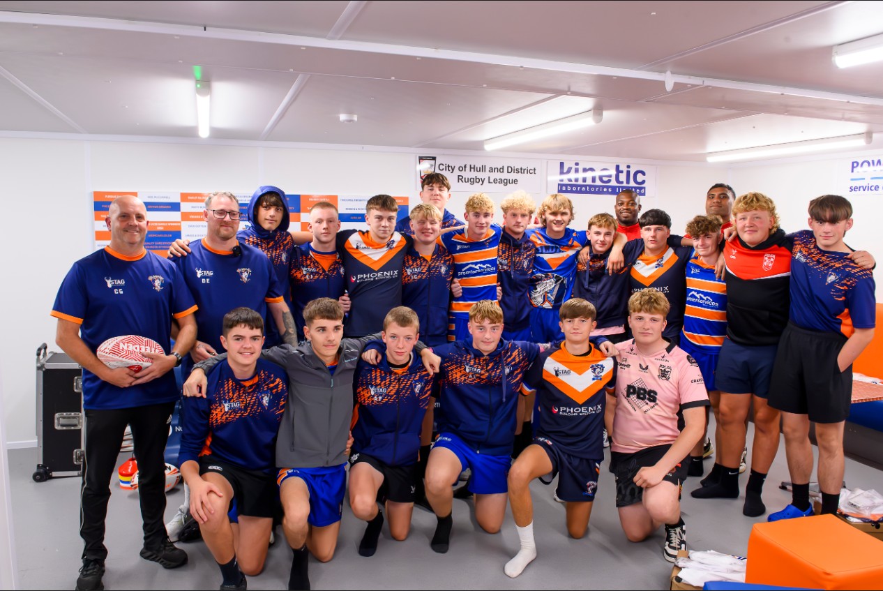 A young rugby team stands with two professional players