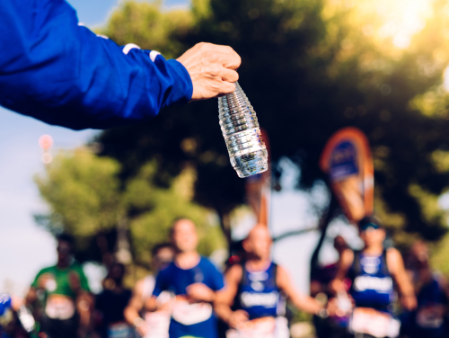 A volunteer holding out a bottle of water to runners during a road race.