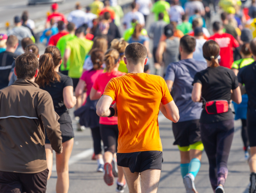 A large group of runners taking part in a road race, with a runner in a bright orange top in the foreground.