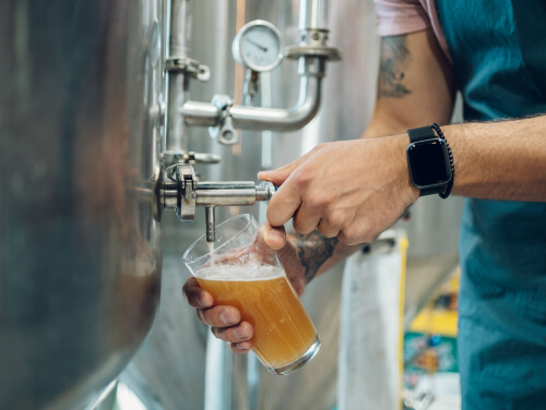 A man pouring himself a beer into a pint glass from a brewery tap.