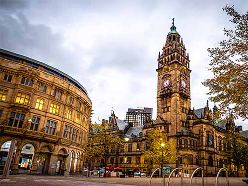 Sheffield Town Hall with clock tower at dusk, surrounded by historic buildings and streetlights.