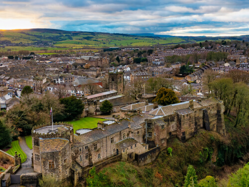 Elevated view of the medieval Skipton Castle, showing its stone towers and fortified walls, with the town and rolling Yorkshire countryside beyond.