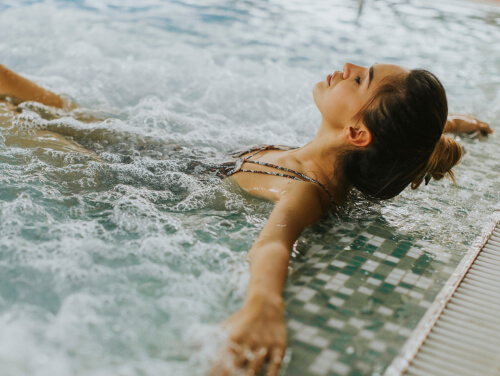 A woman with her eyes closed relaxing back into a bubbling pool of water.