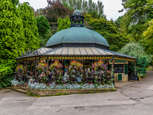 An ornate pavilion with a domed roof in Harrogate’s Valley Gardens, surrounded by colourful flower beds, hanging baskets and lush green trees.