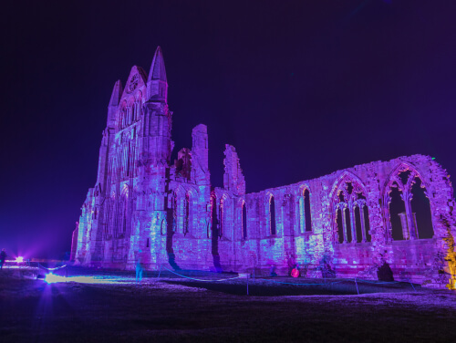 Whitby Abbey illuminated in purple at night to celebrate Halloween.