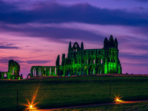 Whitby Abbey illuminated green against a dramatic purple and pink sunset.