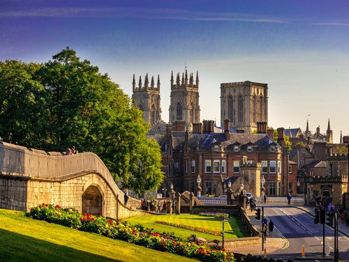 York city view with York Minster in the distance, seen from beside a stone wall and green gardens.
