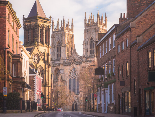 A main street in York on a sunny day with the minster framed by buildings.