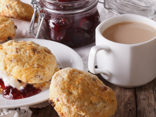 A cup of breakfast tea alongside a jar of jam and scones.