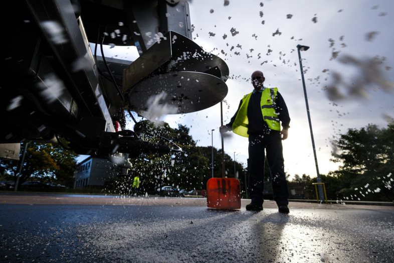 Image of a worker spreading salt on a road surface