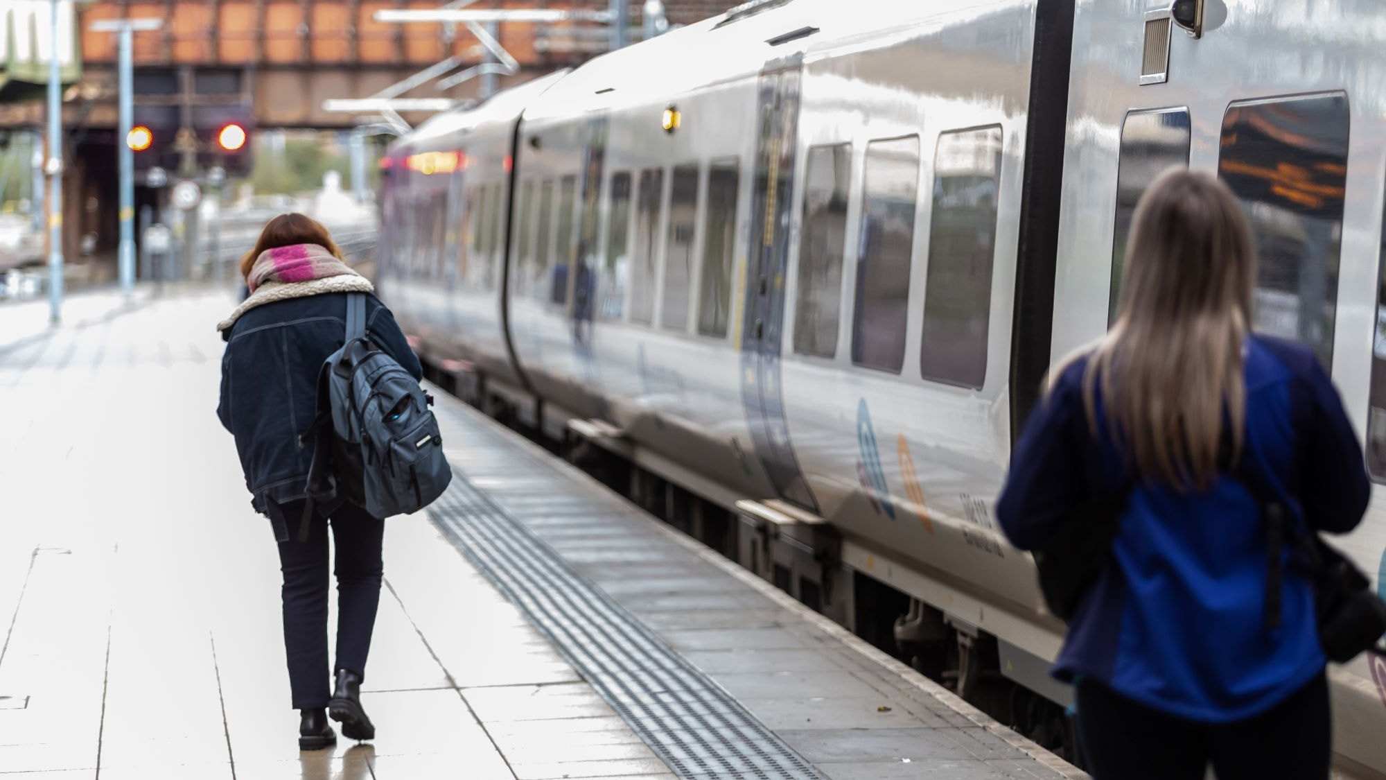 Image shows customer boarding a train as conductor looks on