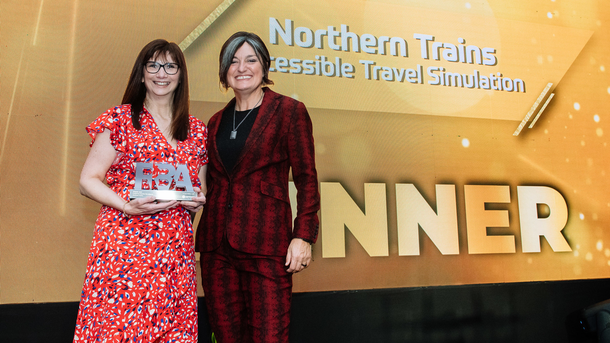 Maxine Myers holding the award with host Zoe Lyons