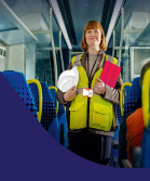 Construction worker on a train, holding her tablet and hat.