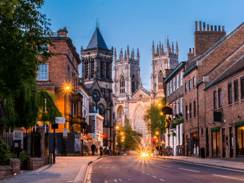 A street in York with a view of the Minster Abbey and beautiful buildings lit up by street lamps
