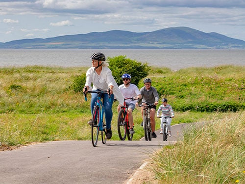 Four adults wearing helmets cycling on a path in the Lake District