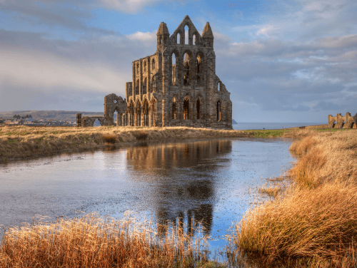 Whitby Abbey with a small body of water in front of it, surrounded by grass